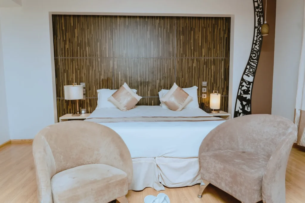 Queen Room with a queen bed against a timber headboard wall, two velvet tub chairs and a carved black screen
