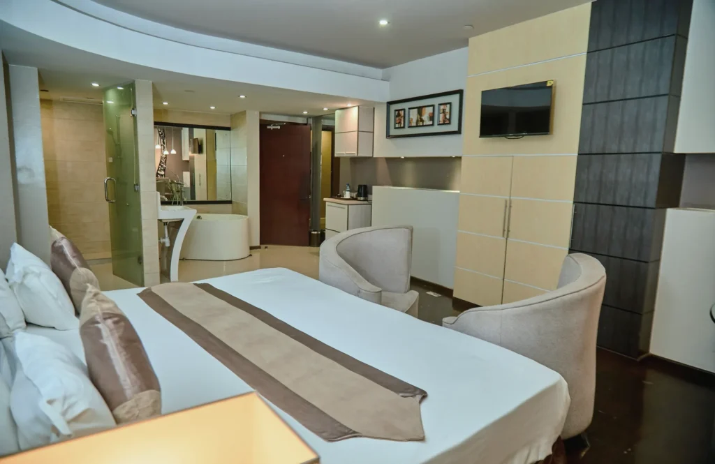 Suite with a king bed, lounge chairs and a glass-walled bathroom with a freestanding tub